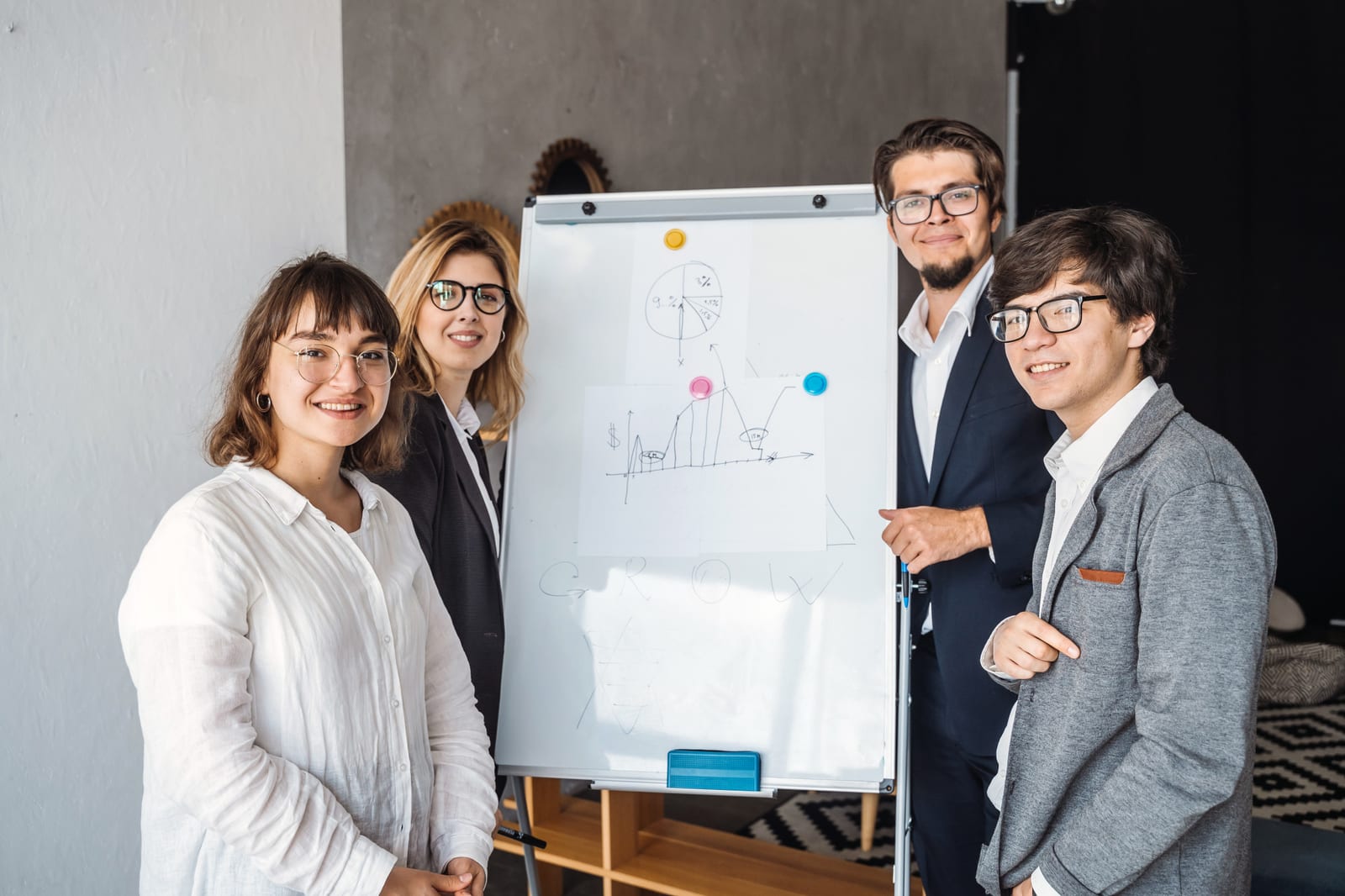 Quatro profissionais sorriem ao lado de um flipchart com gráficos desenhados à mão em uma sala de reunião.